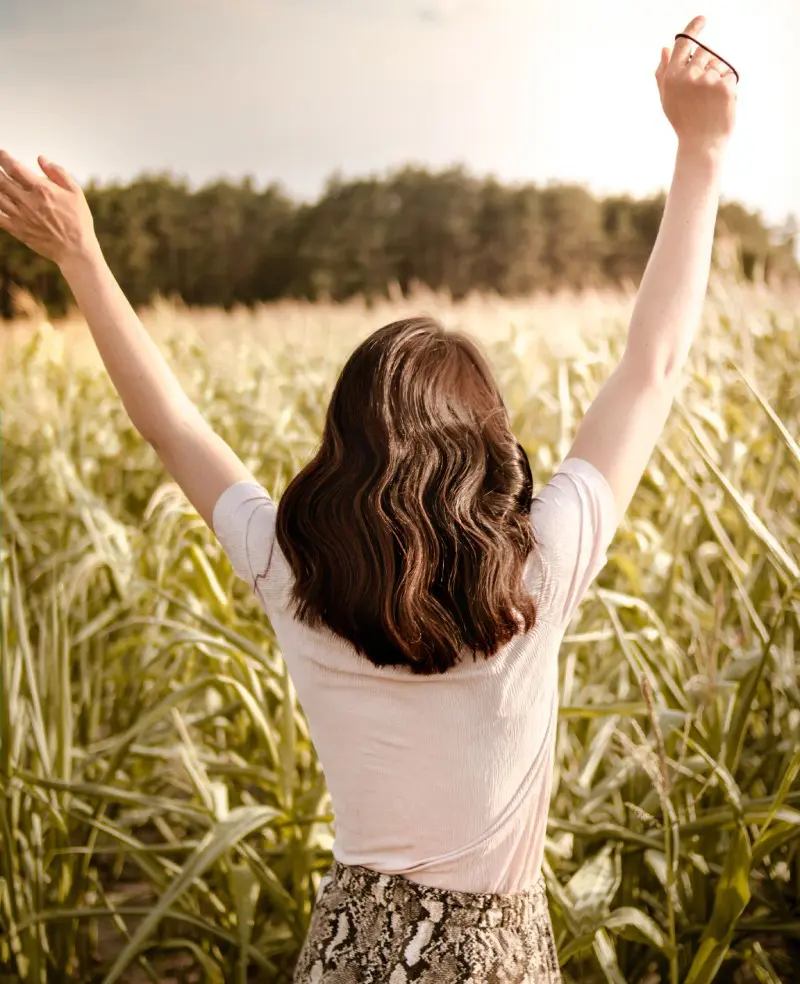 A woman standing in the middle of a field with her arms raised.