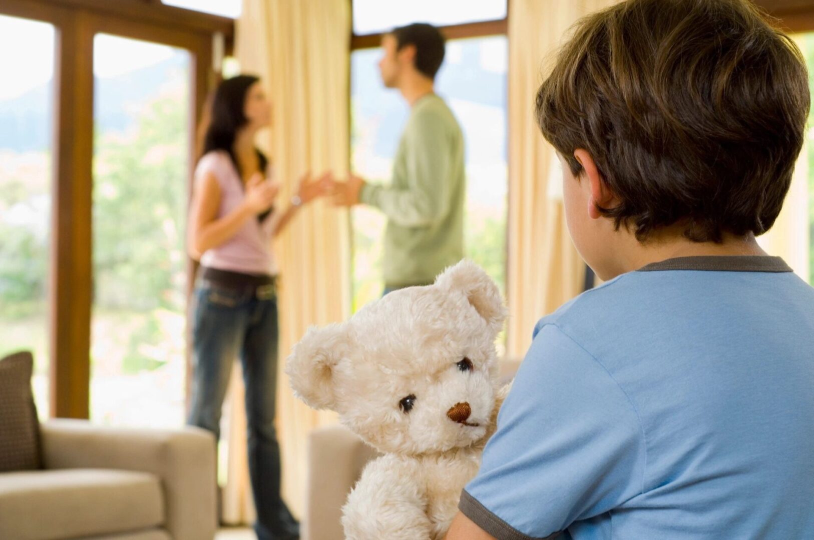 A boy holding a teddy bear in front of two people.